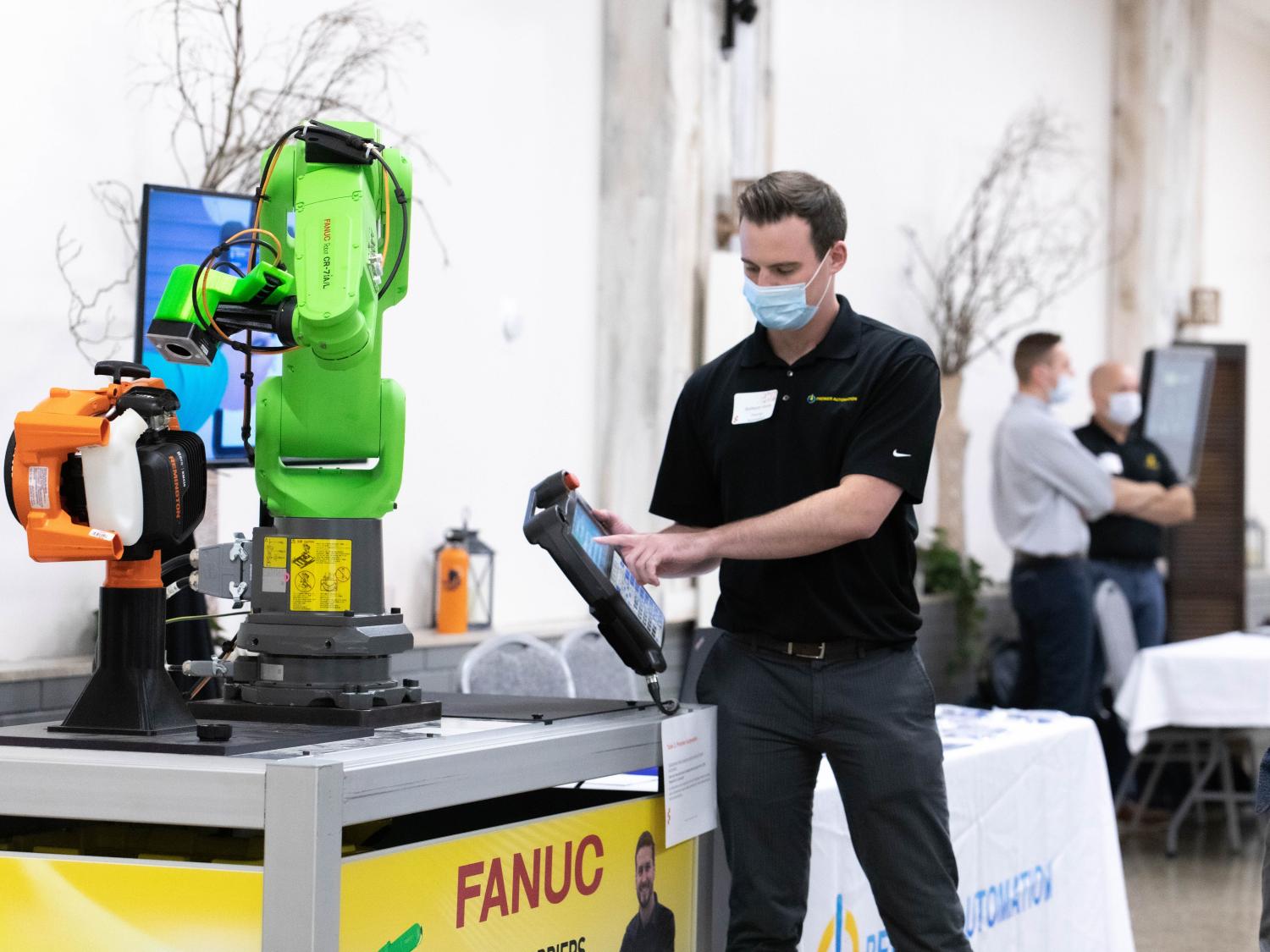 Man wearing mask holds digital tablet in front of robotic arm