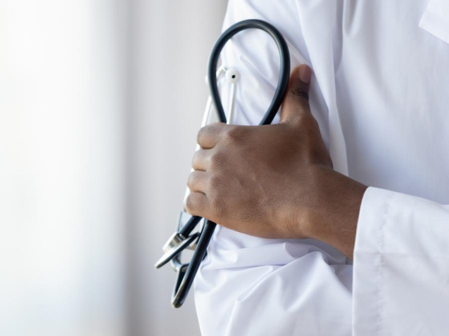 Zoomed-in shot of a person in a physician's coat with their arms crossed, holding a stethoscope in their left hand.