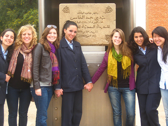 Seven people stand in front of a stone monument.
