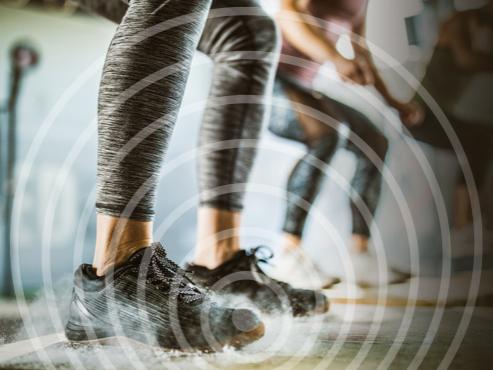 An image of a person's legs in workout clothes and shoes in a squat position, with two other people in a similar position in the background. 
