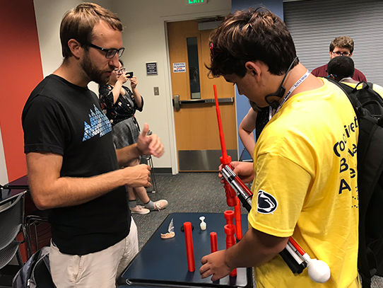 Two men look at red, 3D-printed cylinder pieces. 