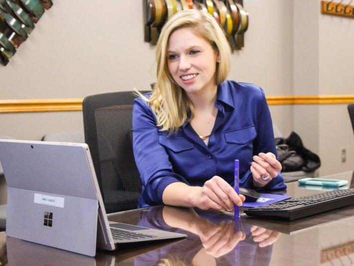 A blonde Caucasian woman interacts with a laptop, talking to someone remotely. 
