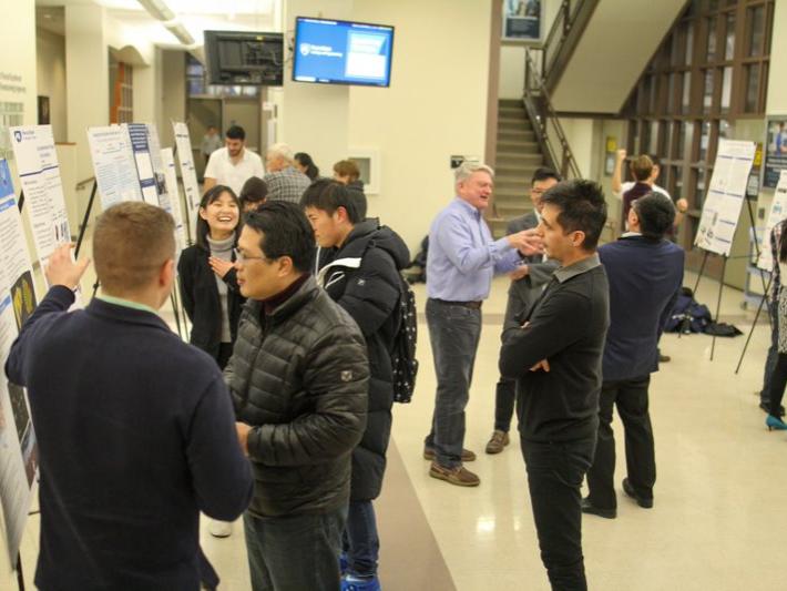 A group gathers in a large lobby area to read and discuss large research posters.