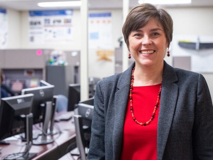 A Caucasian woman stands smiling in a computer lab.