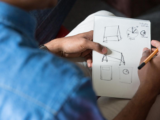 A man's hands hold a piece of paper with circle and triangle sketches. 