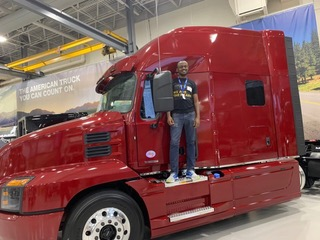 A man stands in front of a large, red tractor-trailer truck.