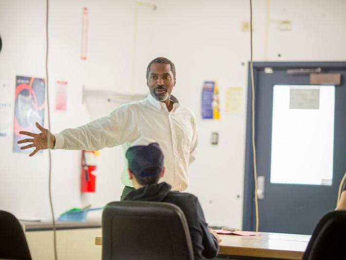 An African American professor gestures in front of an engineering class.