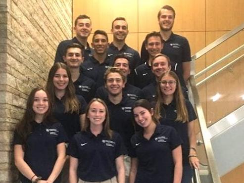 A group of students in blue Penn State polo shirts posing on steps. 