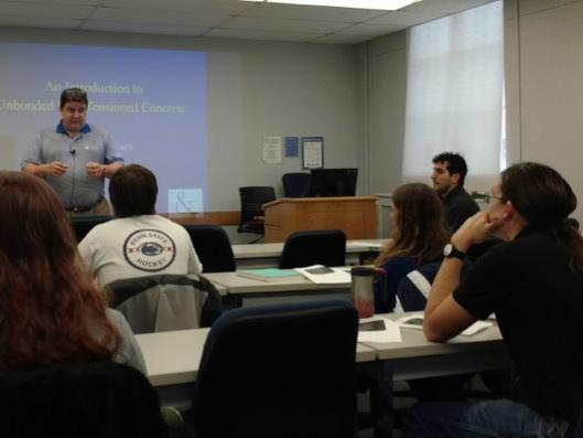 A man stands and speaks in front of a classroom of students. 