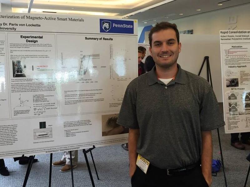 A male graduate student stands in front of a poster detailing research.