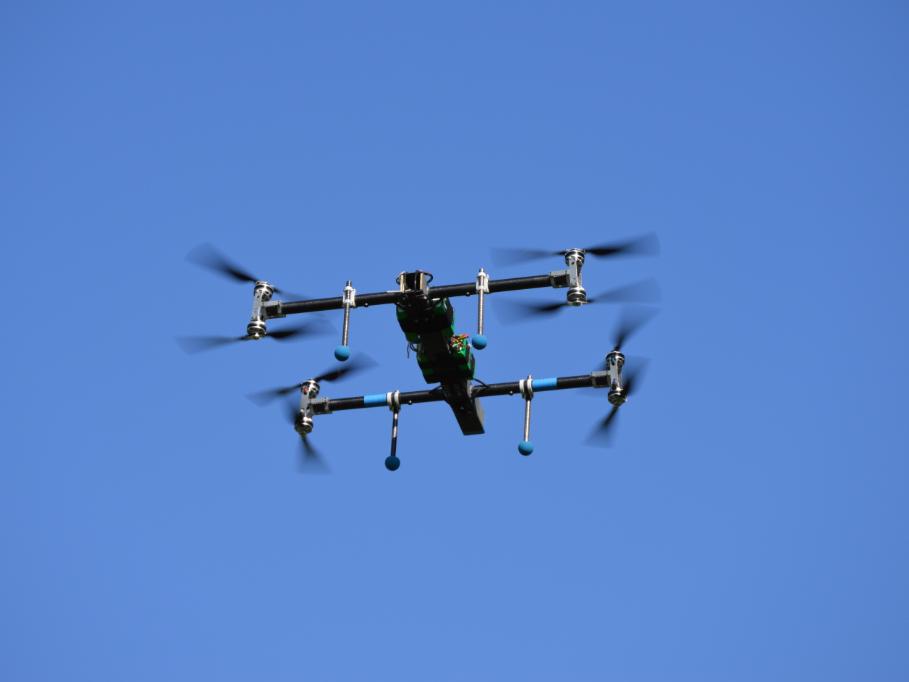 A small quadcopter flies against a blue sky. 