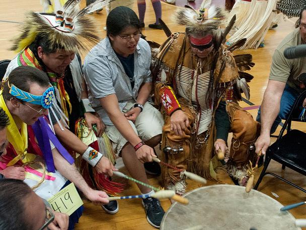 American Indians in full dress gather around a drum during a powwow.