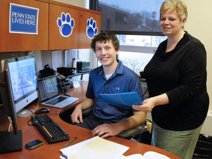 student at desk with woman standing behind him