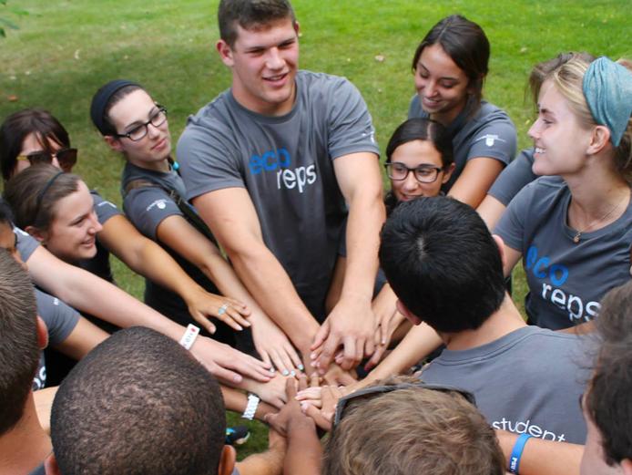 Students with "eco rep" t-shirts put all hands in while standing in a circle.