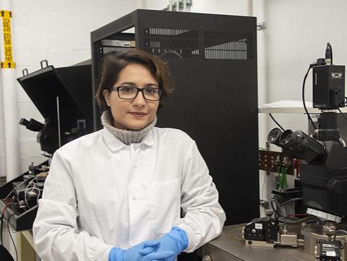 A professor in glasses stands in front of testing machinery in her lab. 