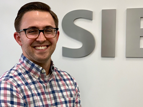 Person stands in front of a wall and smiles