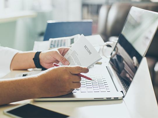 Image of person sitting at a desk reviewing resume over a laptop