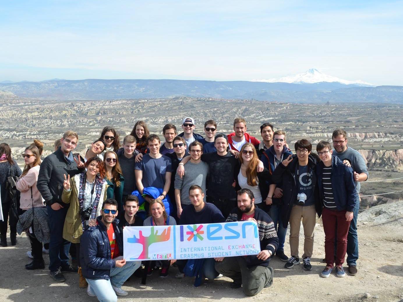 group of students standing for a photo on a cliff with beautiful landscape behind them