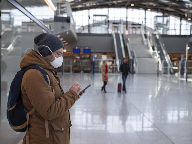 A man wearing a face mask stands alone in a railway station while using his smartphone