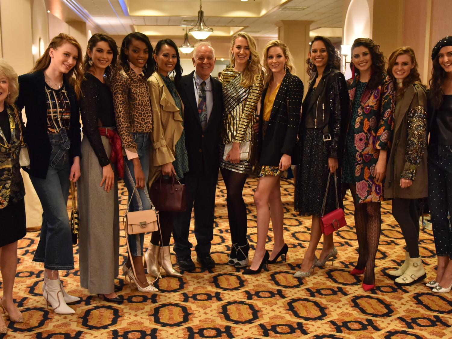 Jeanne and Ed Arnold smile with 10 models at the 2018 Neiman Marcus Runway Show. The models wear a variety of fashions and stand in a row on an ornate carpet.