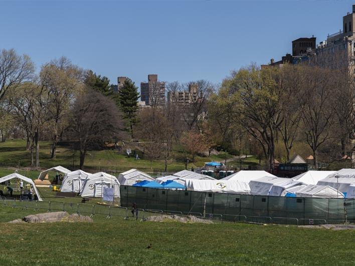 Tents sat on a green field with cityscape in the background.