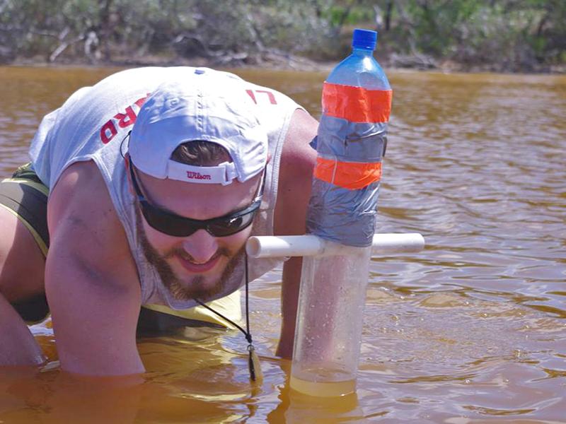 Penn State student Tyler Betz crouched in a brown salt lake, collecting a mud core for research.