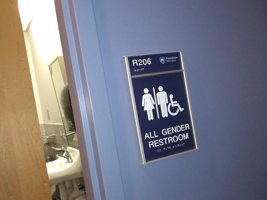 A partially open door to a single-stall bathroom with a sign stating "All Gender Restroom"