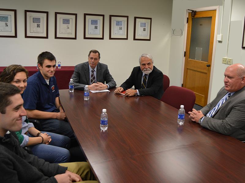 students and faculty sitting at table talking to congressman