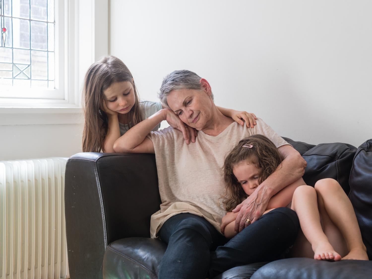sad grandmother on couch with 2 granddaughters