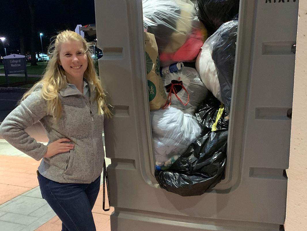 A young woman stands next to a large bin full of bags of winter coats.