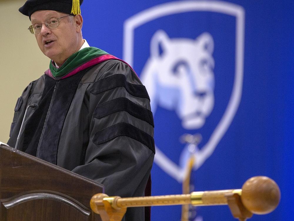 Dr. Craig Hillemeier stands at a podium and speaks. Behind him, the Nittany Lion logo is visible on a banner.