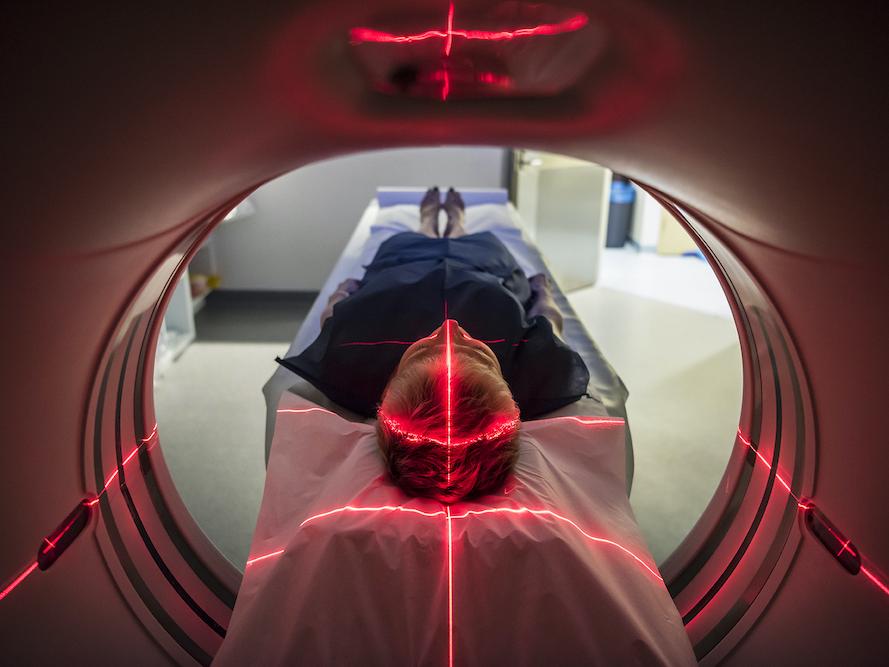 A woman enters an MRI machine with red laser lights covering her head and torso. 