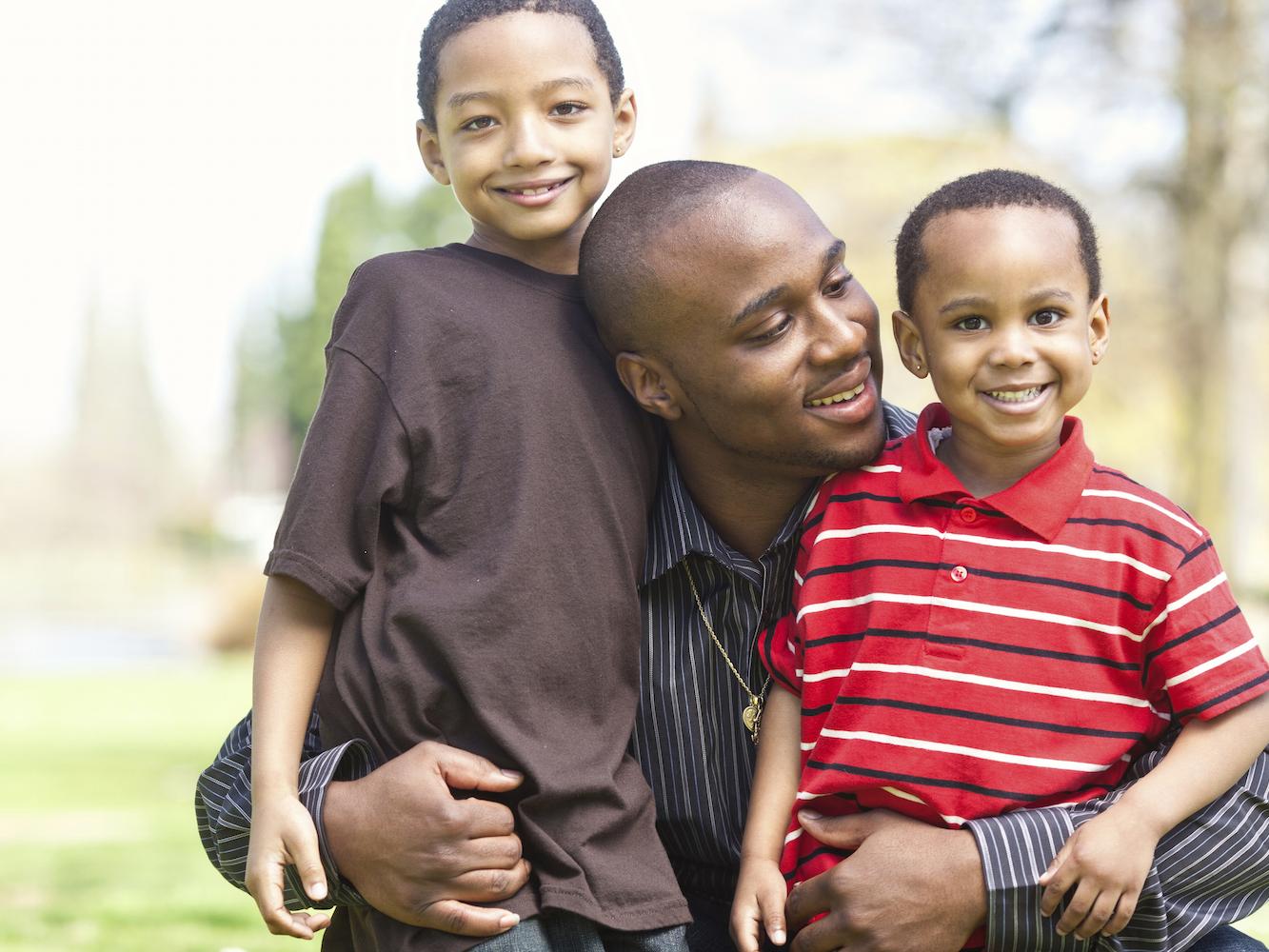 Two young African American boys hugged by father