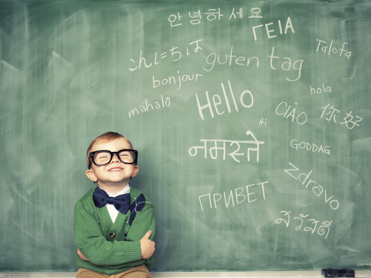 child in front of chalkboard with several languages on it
