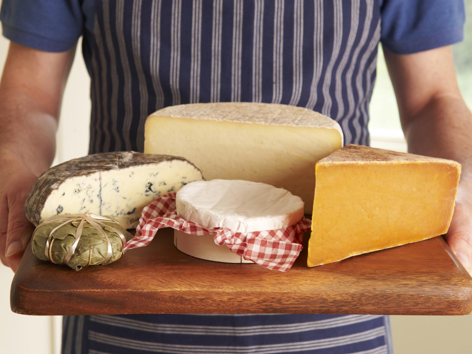 Grocer Holding Board With Selection Of Luxury Cheeses