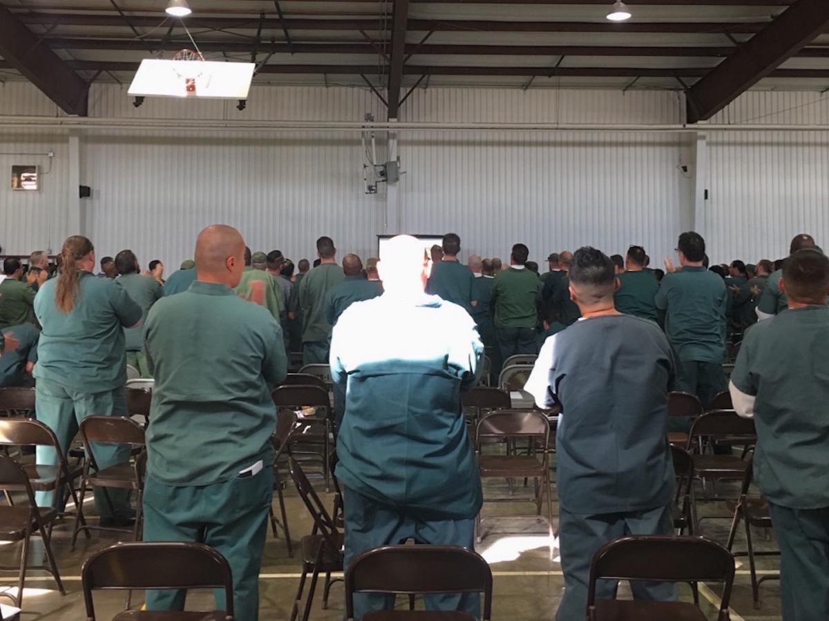 Inmates in Indiana stand in a common room to listen to a speaker.