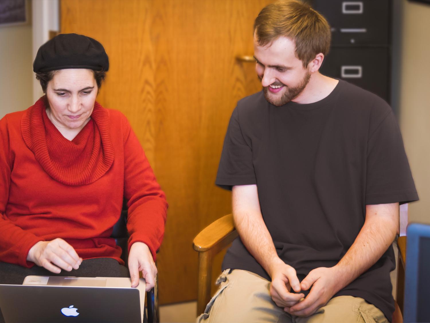 Professor and student sit next to each other looking at laptop