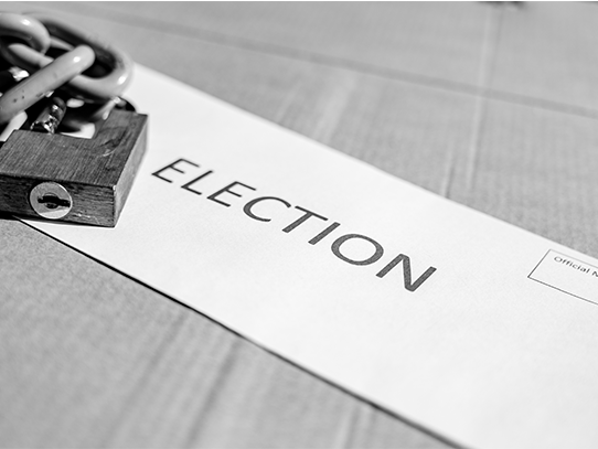 Black and white photo of an envelope stamped with the word election and a lock and linked chain of top of it.