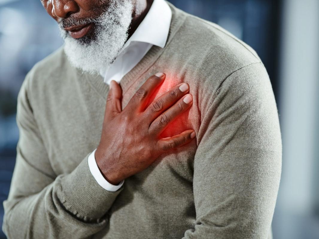 A man wearing a sweater places his right hand over his heart, apparently in chest pain.