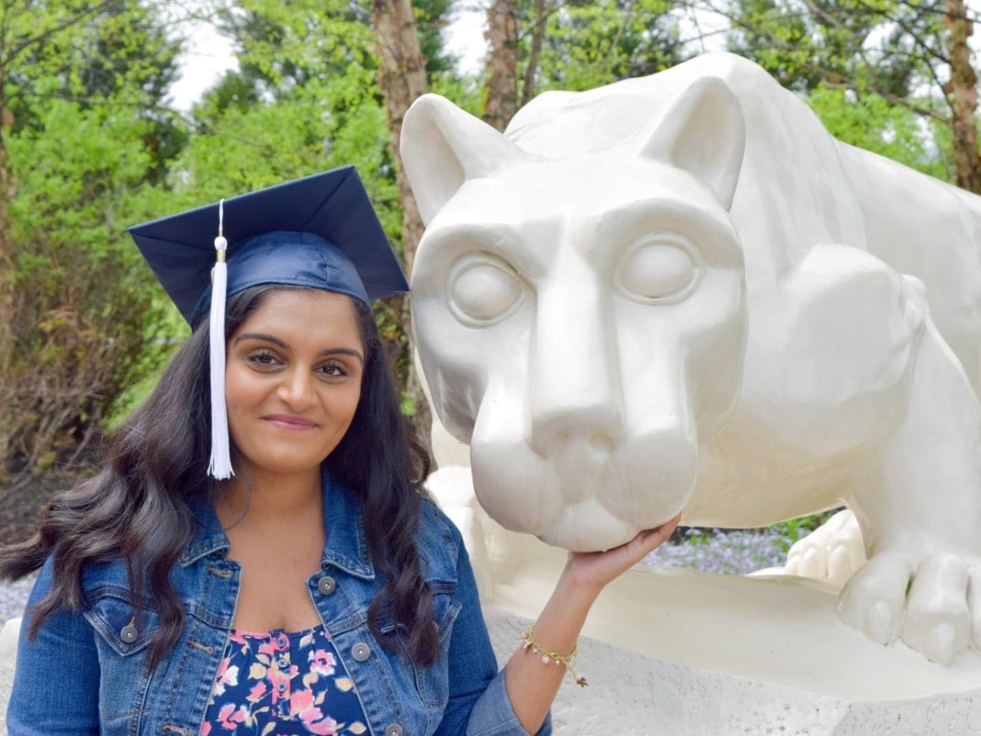 female student in cap and gown at Nittany Lion shrine