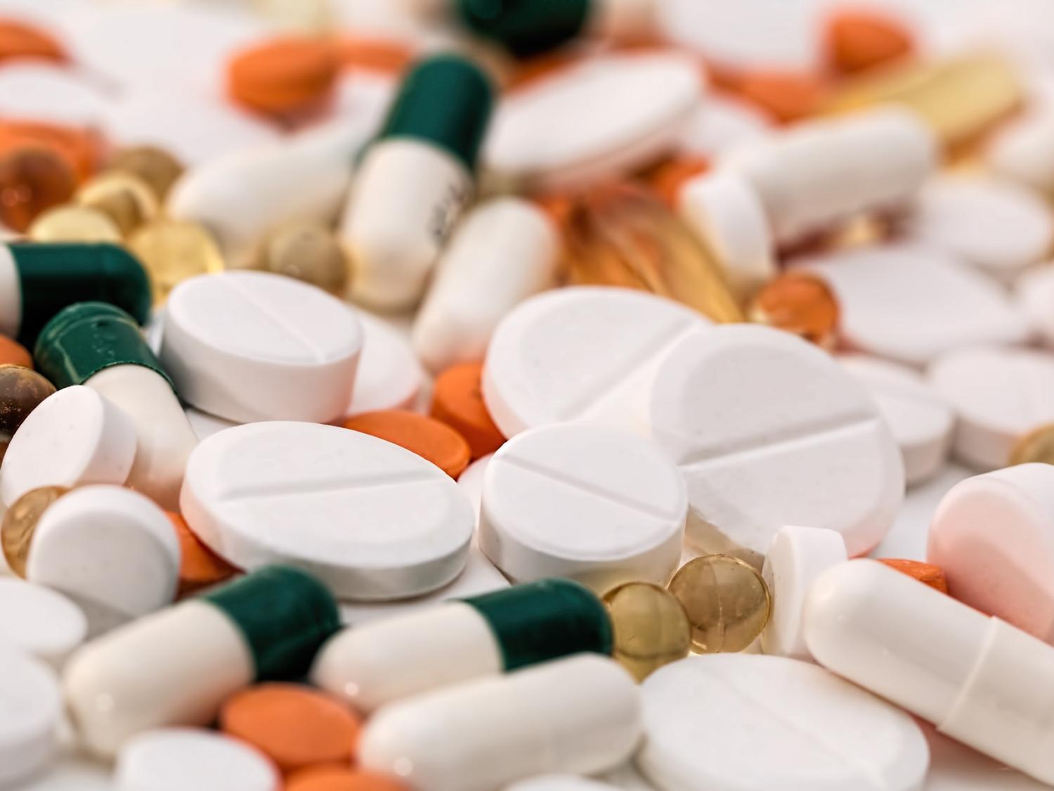 A close-up of a pile of medication, including white pills, orange pills and green and white capsules.