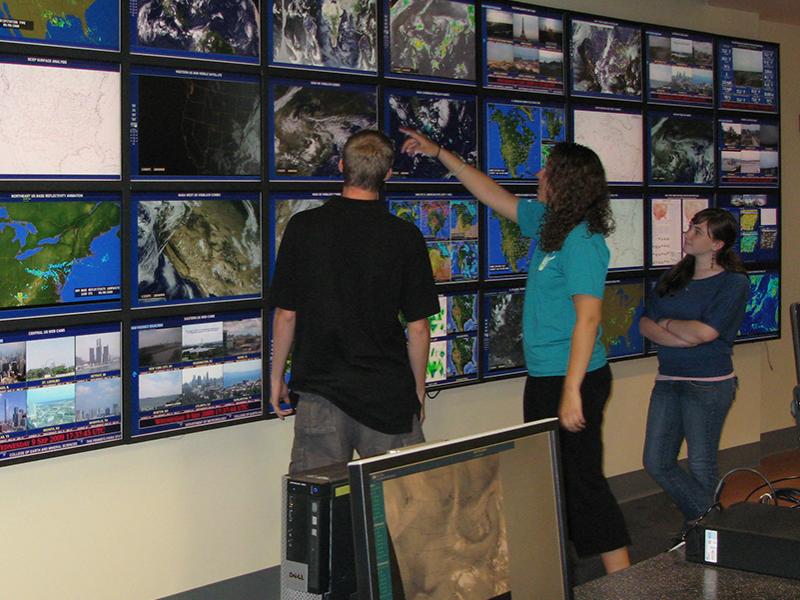 meteorology students stand at Joel Myers weather wall