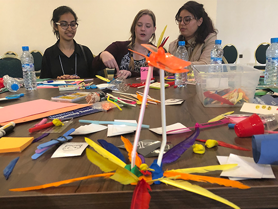 Three people sit at a table covered in craft supplies.