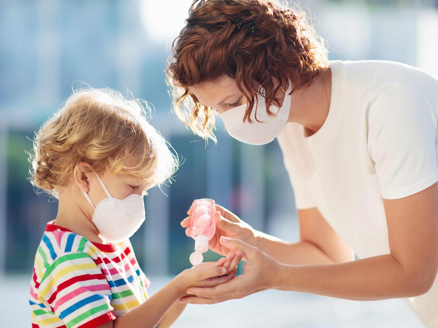Mother applying sanitzer to child, both are wearing face masks