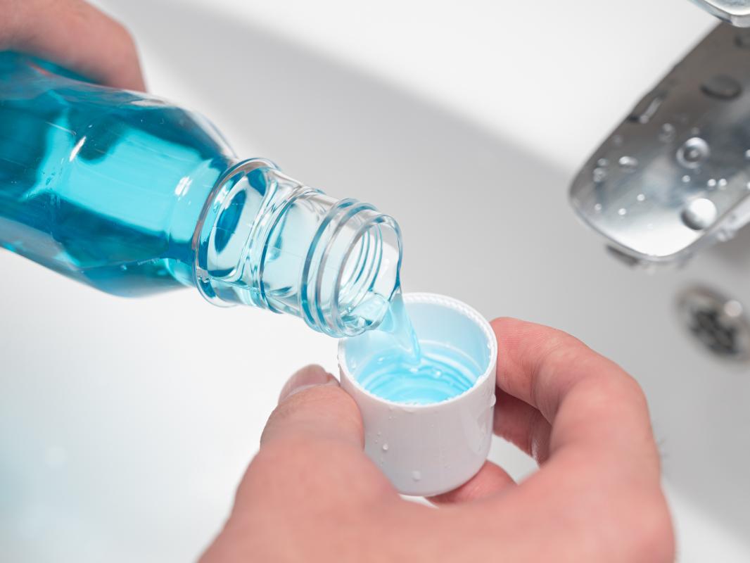 Blue mouthwash is poured into a white cap over a white sink. 
