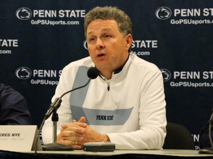 Penn State men's golf coach Greg Nye speaks at the microphone on the dais at fall sports media day