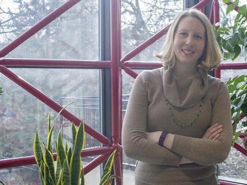 A professor stands in front of greenery smiling. 