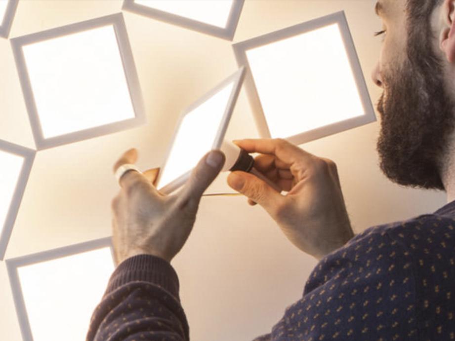A man holds an organic LED luminaires in front of a wall that contains several more identical luminaires