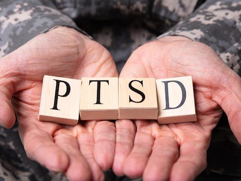 soldier's hands holding scrabble blocks spelling out PTSD