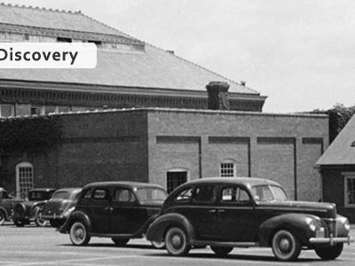 black and white photo of ivy covered brick buildings with antique cars parked in the front